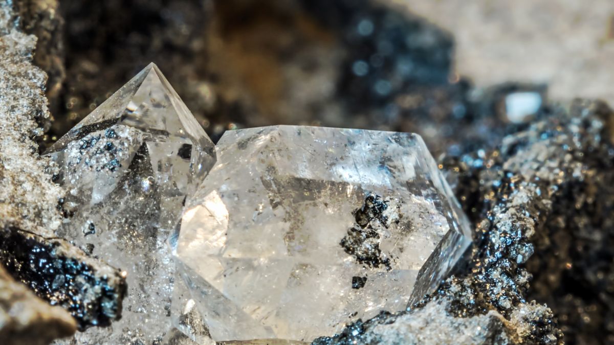 Két Herkimer gyémánt kristály, csillogó felülettel, sötét ásványok között.