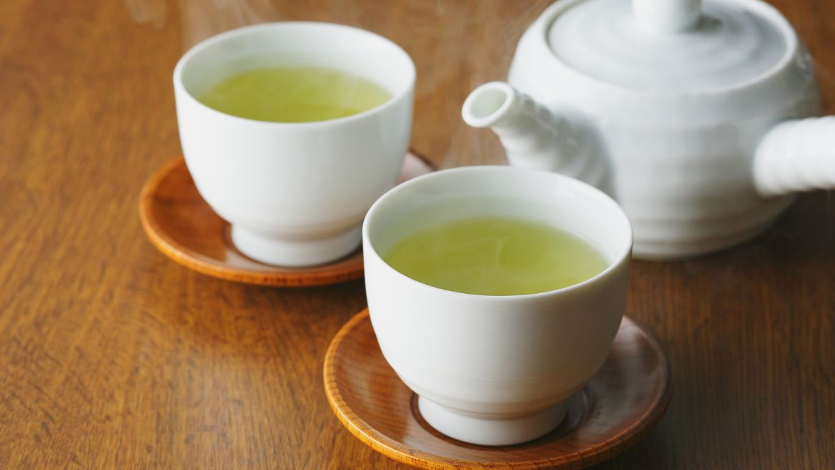 Két gőzölgő csésze jiaogulan tea fehér porcelánban, mellette egy teáskanna.