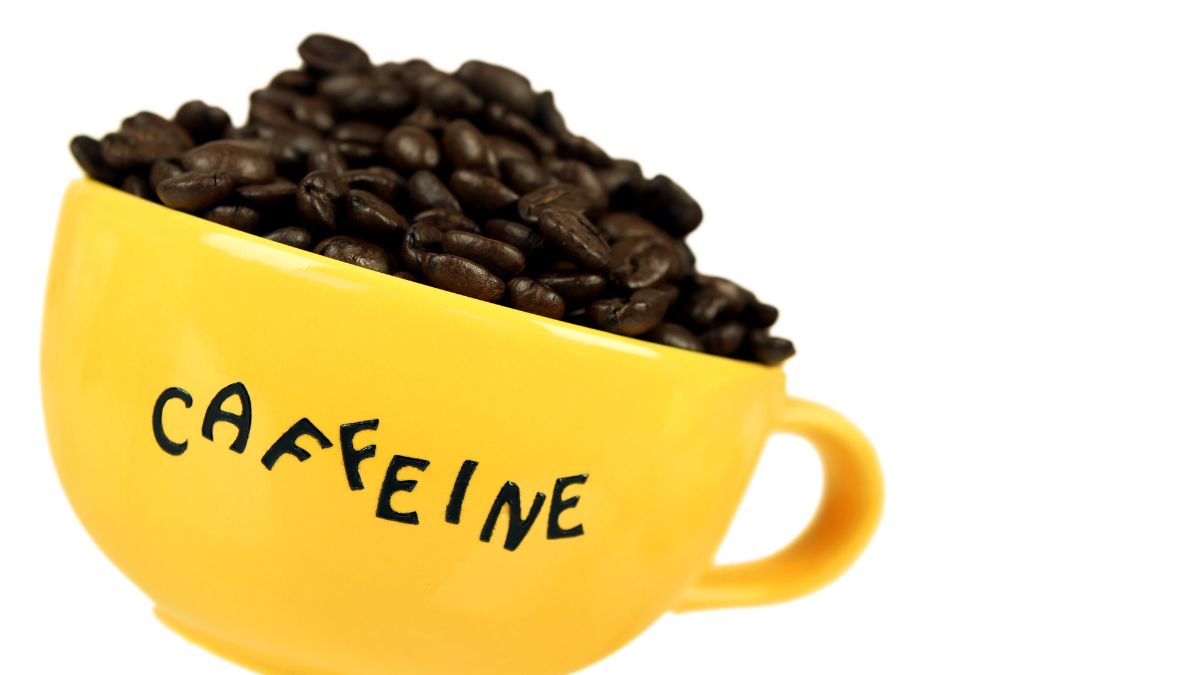 Egy sárga csésze tele frissen pörkölt kávébabbal, a koffein szimbóluma.