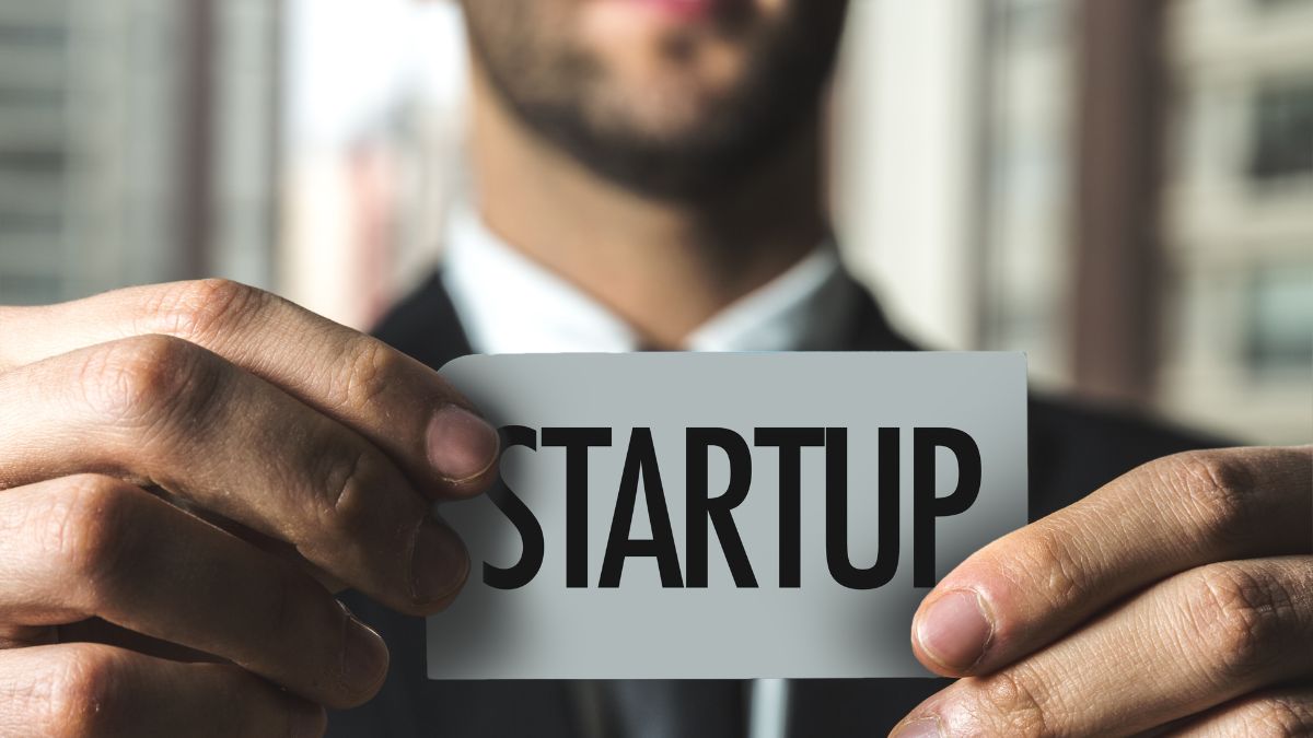 Egy férfi egy startup feliratú névjegykártyát tart a kezében, üzleti környezetben.