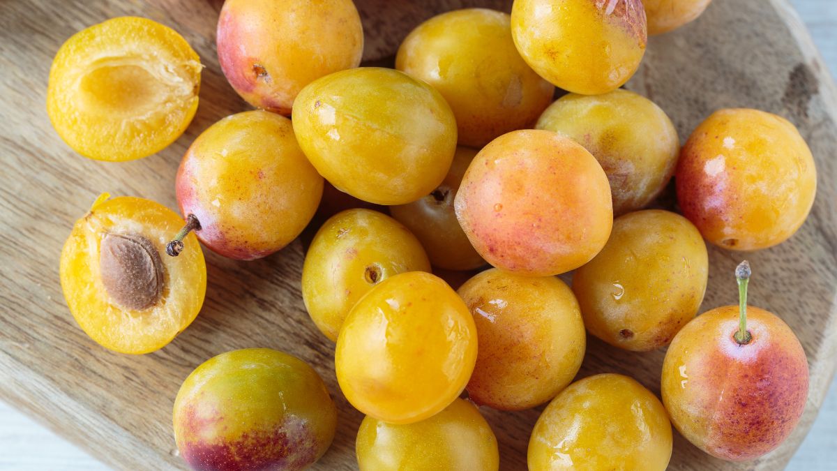 Friss mirabella szilvák, sárgás-narancssárga színben, egy fából készült tányéron.