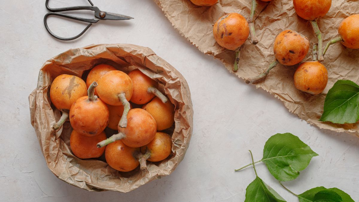 Friss naspolya gyümölcsök egy papírból készült kosárban, zöld levelekkel.