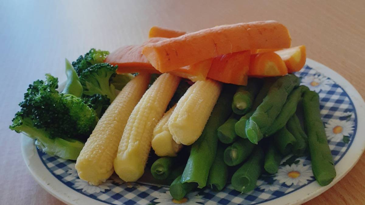 Friss zöldségek, köztük brokkoli, sárgarépa, zöldbab és baby kukorica egy tányéron.