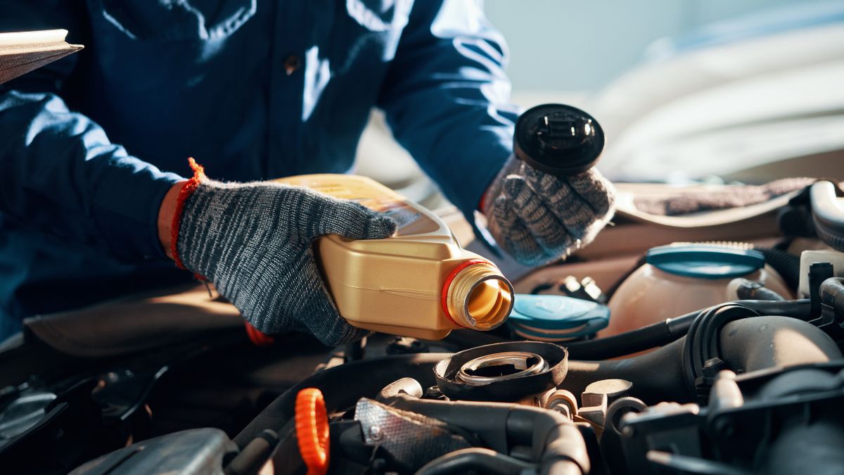 Egy autószerelő olajat önt egy motorba, miközben a motor alkatrészeit ellenőrzi.
