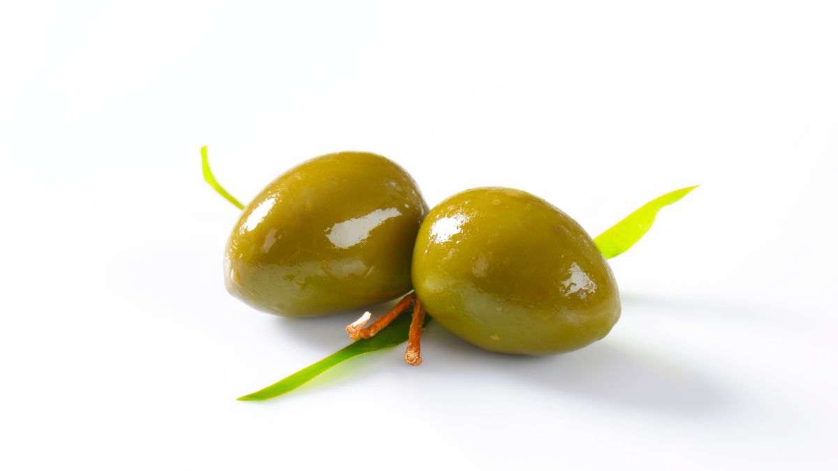 Két zöld olivabogyó, friss levelekkel, világos háttér előtt.