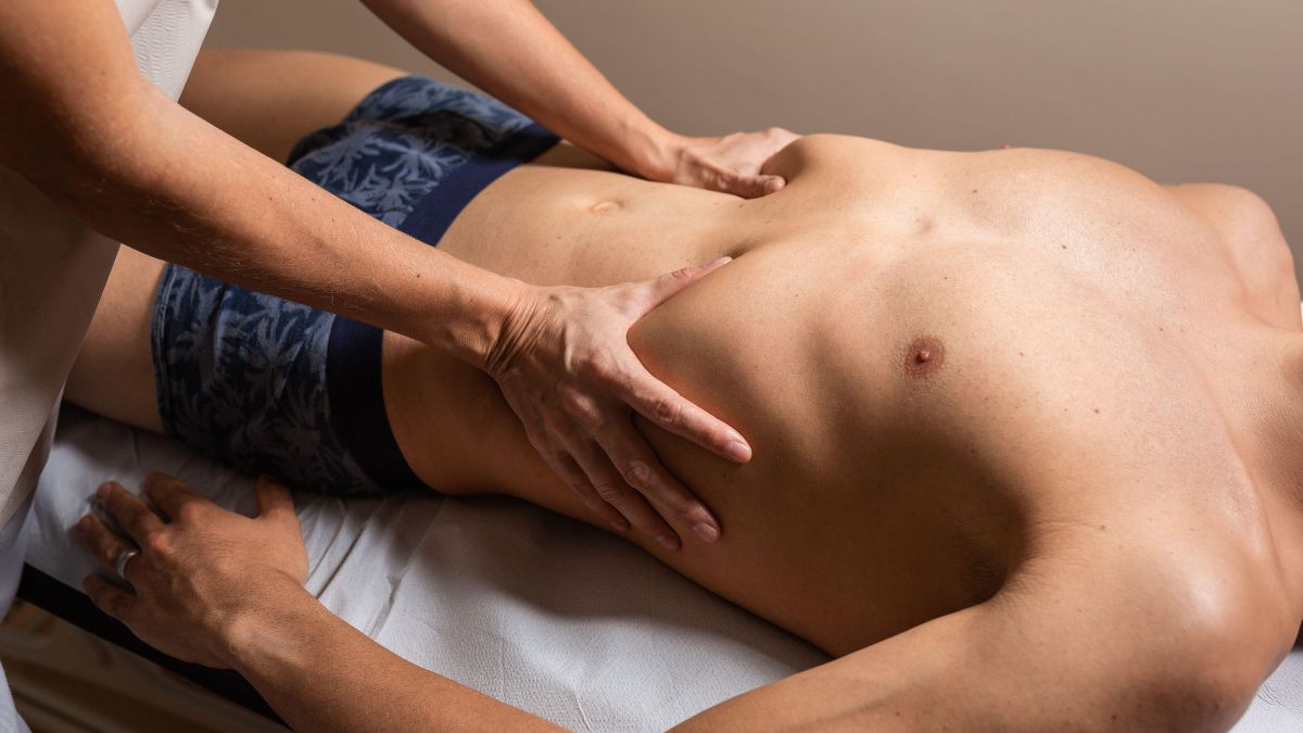 Egy masszőr kezével a rekeszizom területén végez kezelés egy fekvő férfin.