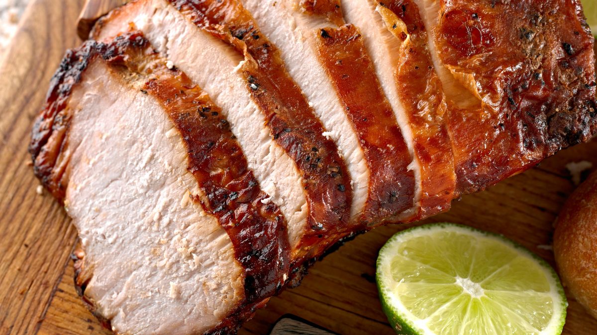 Szeletelt sült sertéshús, mellette lime szeletek egy fából készült tányéron.