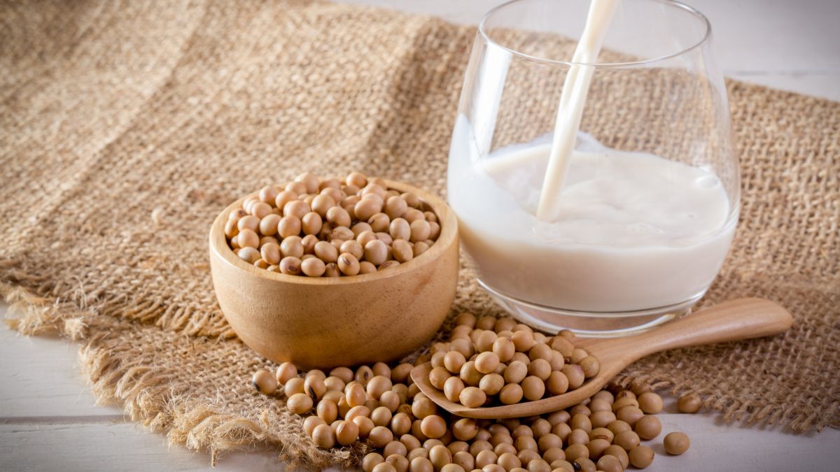 Szója szemek egy fából készült tálban, mellette szója tej egy pohárban.