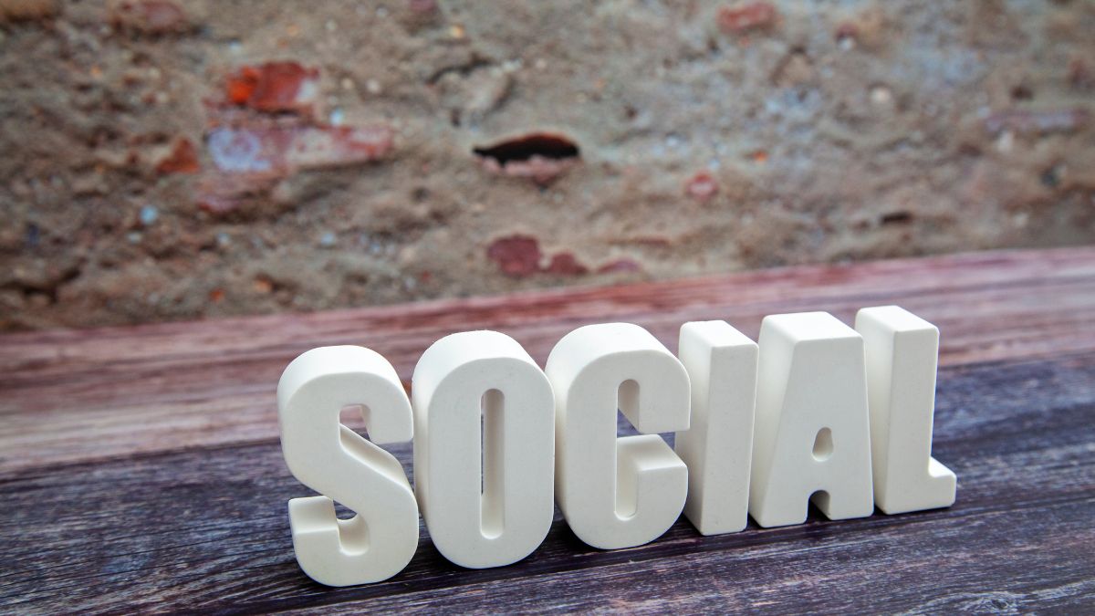 A 'SOCIAL' felirat fehér betűkből, fa asztalon, háttérben téglafal.