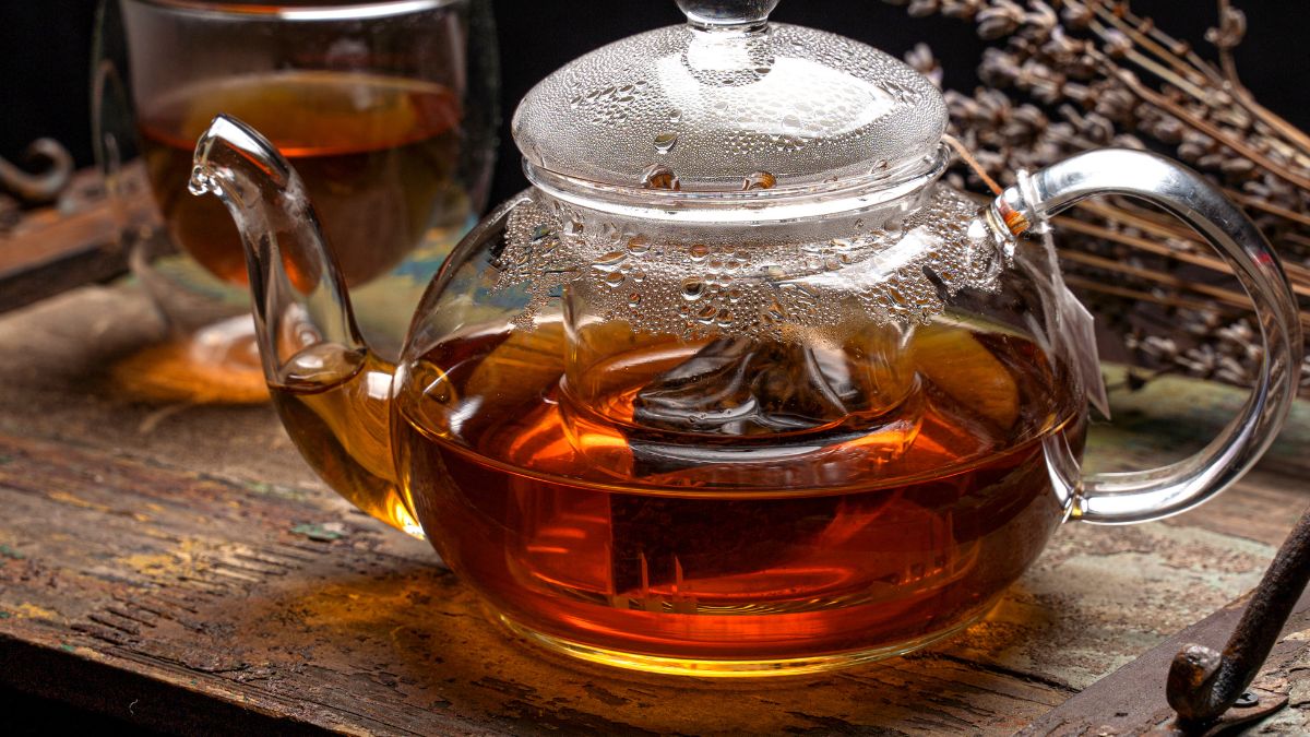 Egy üveg teáskanna gőzölgő teával, háttérben egy csésze tea és szárított levendula.