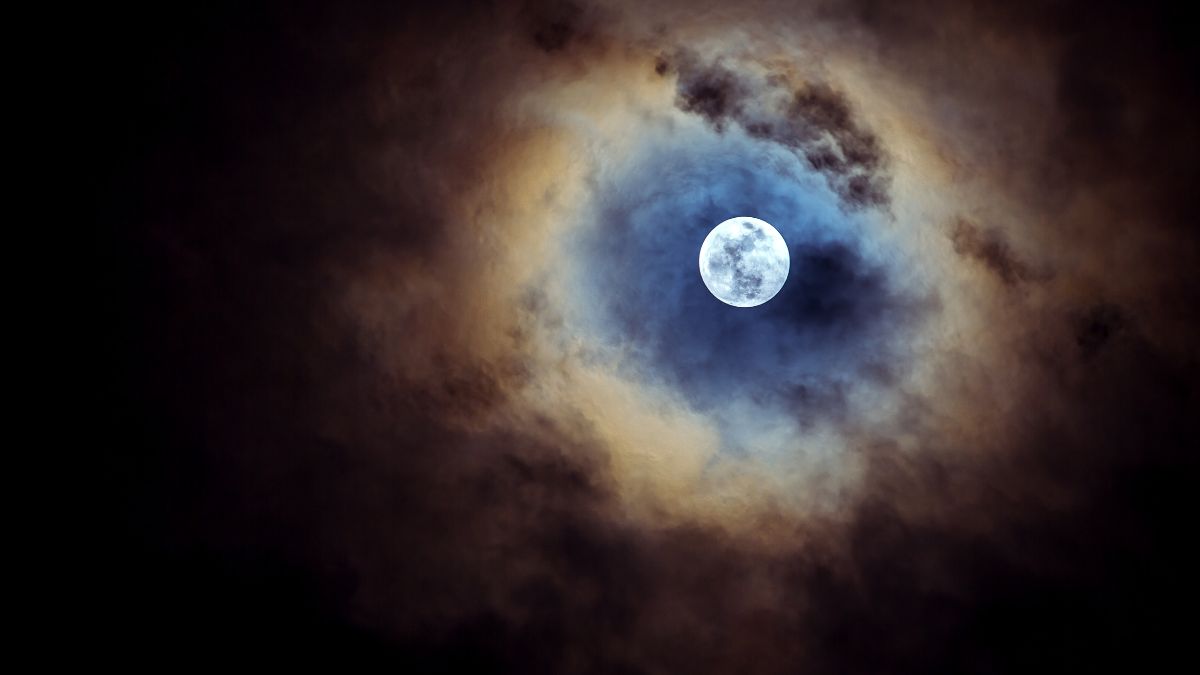 Telihold ragyog a sötét felhők között, misztikus fényjátékkal.