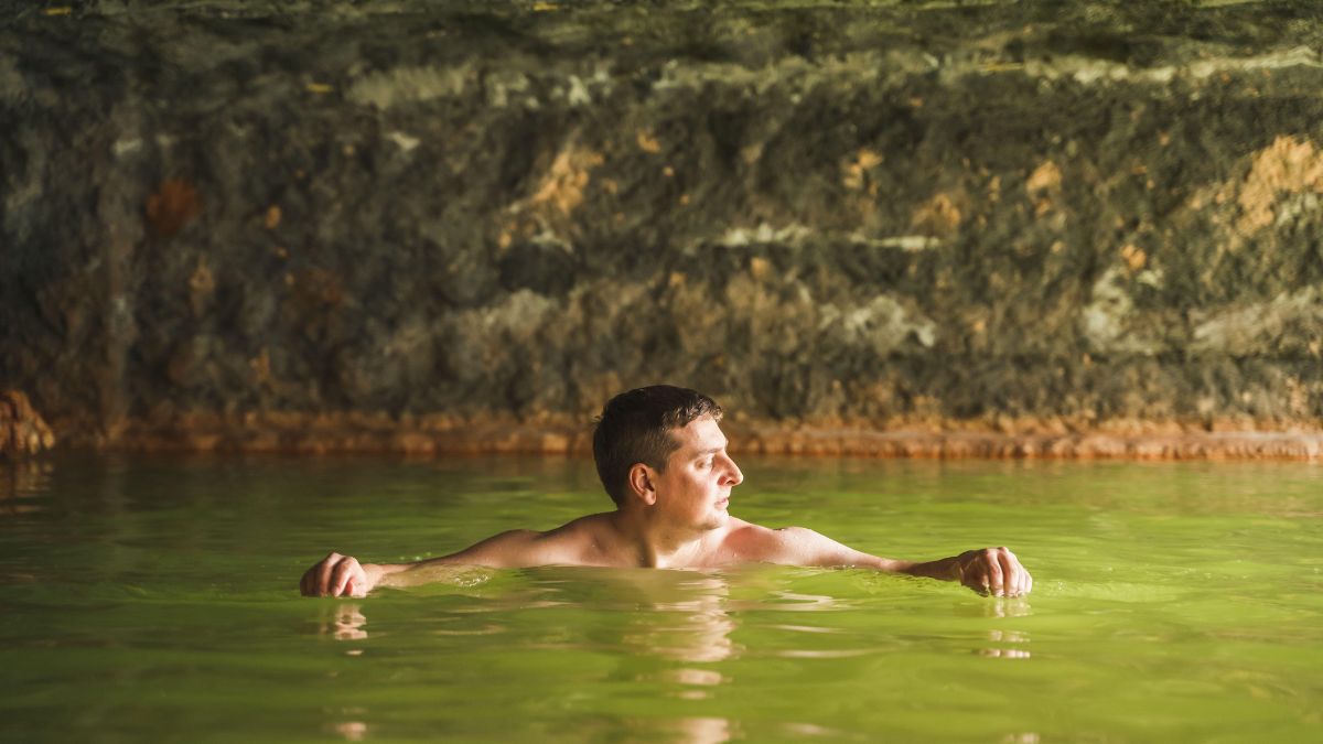 Egy férfi relaxál a termálvízben, amely zöldes színű és természetes környezetben található.
