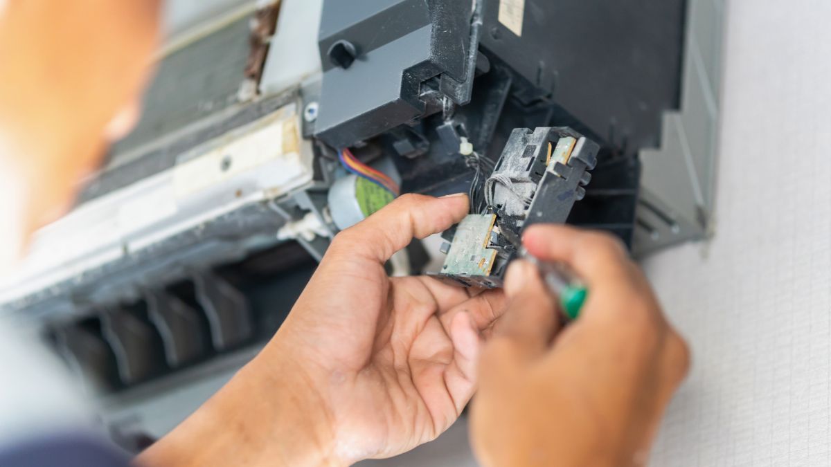 Egy technikus termisztort szerel egy elektronikai eszközbe, miközben csavarhúzót használ.