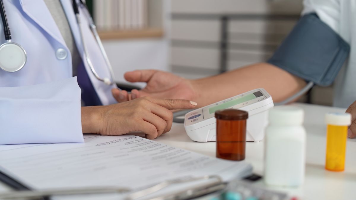 Orvosi vizsgálat során vérnyomásmérő készülék használata, gyógyszerek a háttérben.