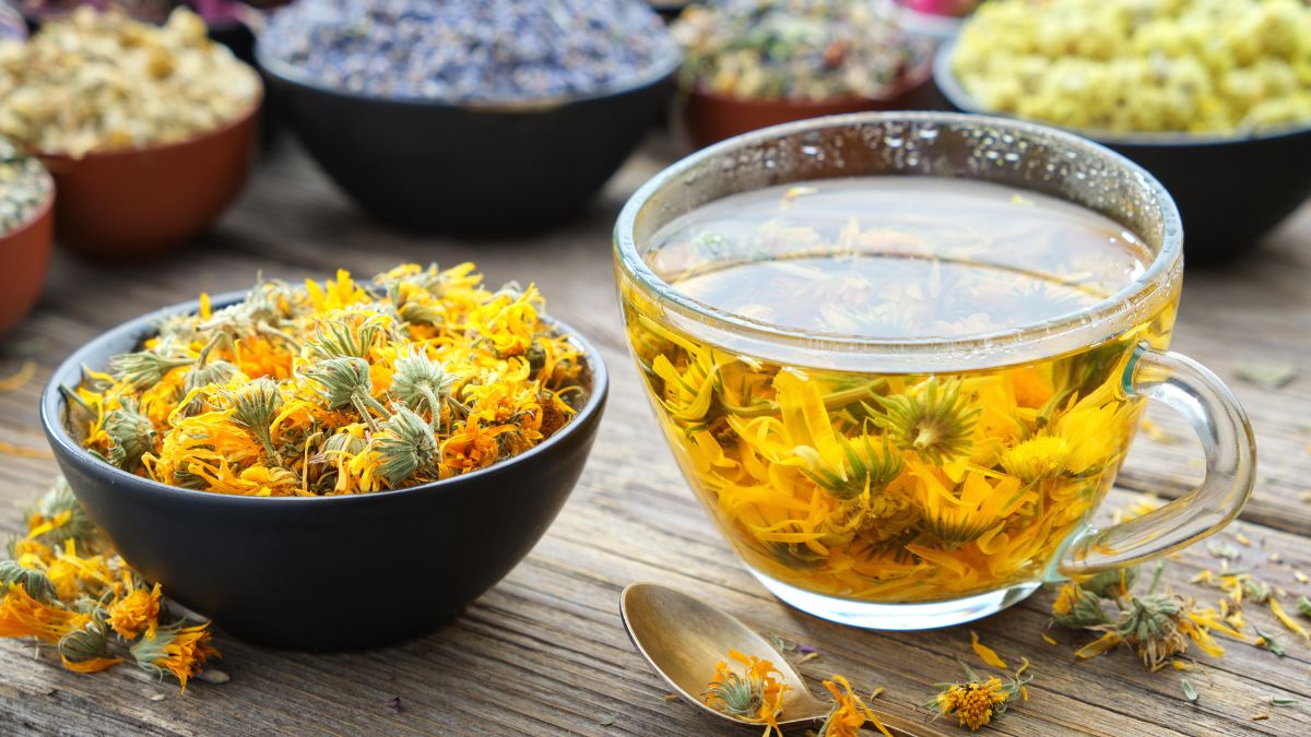 Körömvirág tea egy átlátszó bögrében, körülötte szárított körömvirág virágok.