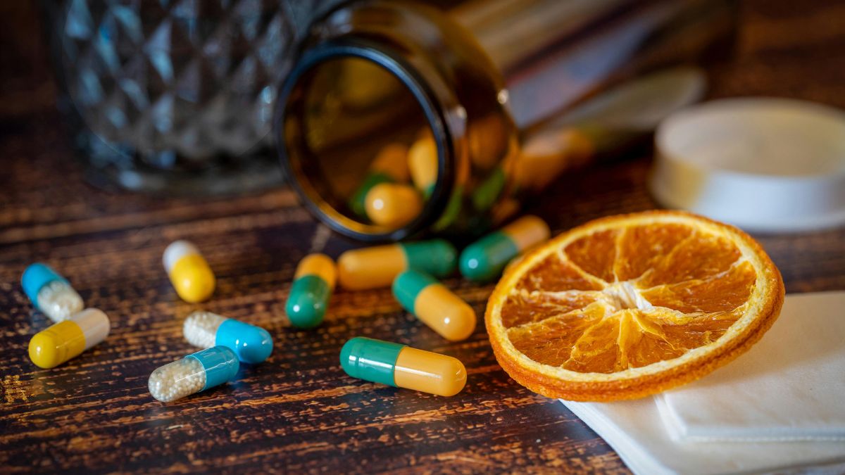 Különböző színű vitamin kapszulák és egy szárított narancs szelet egy asztalon.