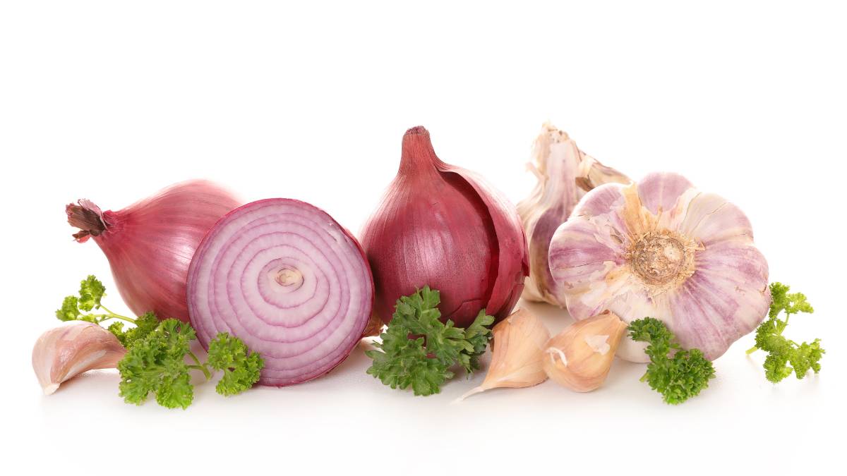 Vöröshagyma, fokhagyma és petrezselyem friss zöldségek egy fehér háttéren.