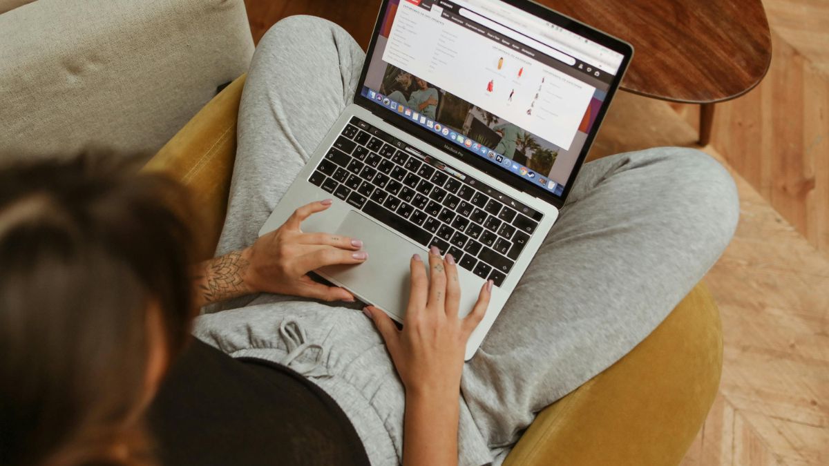Egy fiatal nő ül egy kanapén, laptopján a Wish webáruházat böngészi.