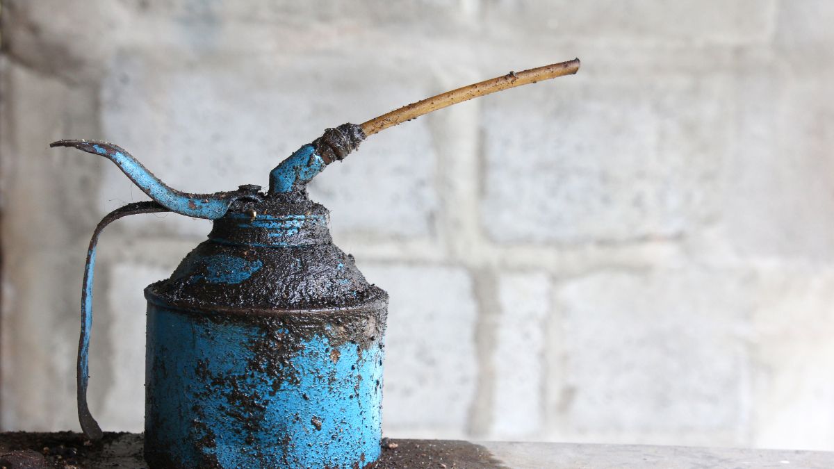 Egy régi, kék kézi zsírzó, amely olajjal van borítva, háttérben szürke fal.