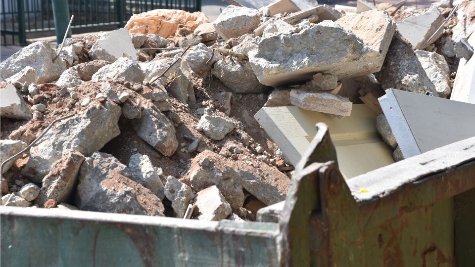 Egy konténer tele építési törmelékkel, köztük betondarabokkal és faanyaggal.