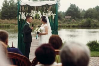 Letisztult esküvői ceremónia a természetben, fehér virágokkal és zöld háttérrel.