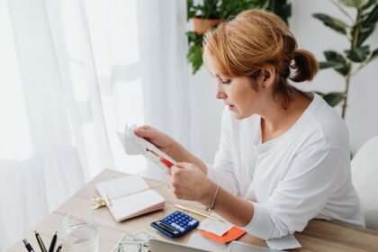 Nő átutalási bizonylatokat kezel, íróasztalon számológép és notesz.