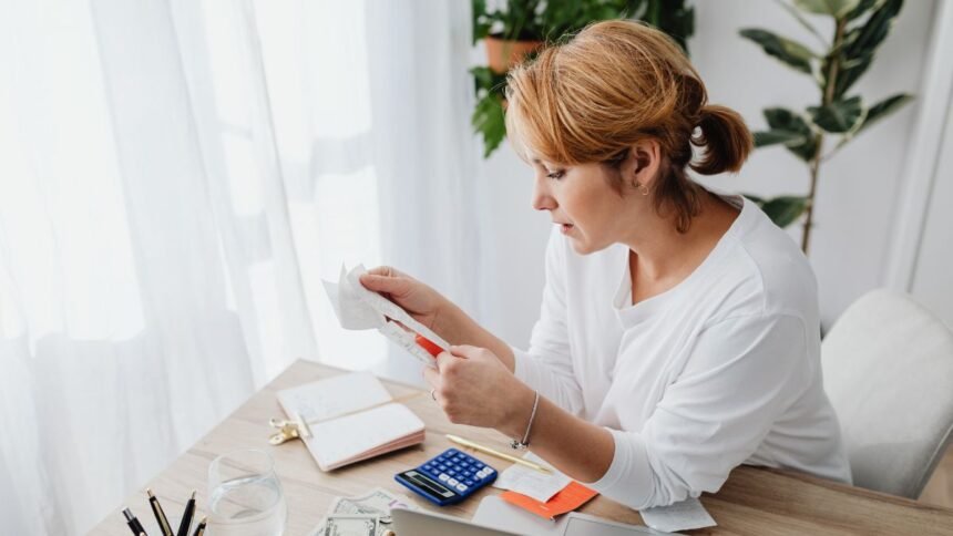 Nő átutalási bizonylatokat kezel, íróasztalon számológép és notesz.