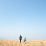 Pár sétál a homokos tájon, kék ég alatt.