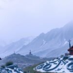 Hegyek és piros házak ködben, nyugodt tájjal.