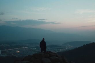 Férfi hegytetőn, a város és a hegyek panorámájával a háttérben.