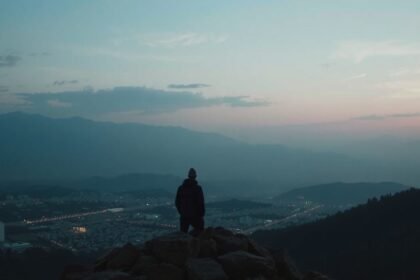 Férfi hegytetőn, a város és a hegyek panorámájával a háttérben.