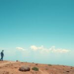 Egy férfi sétál egy hegyvidéki tájon a felhők alatt.