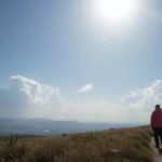 Napsütés és felhők felett sétáló ember a dombon.