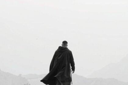 Férfi hátulról fekete köpenyben, tájban barangolva