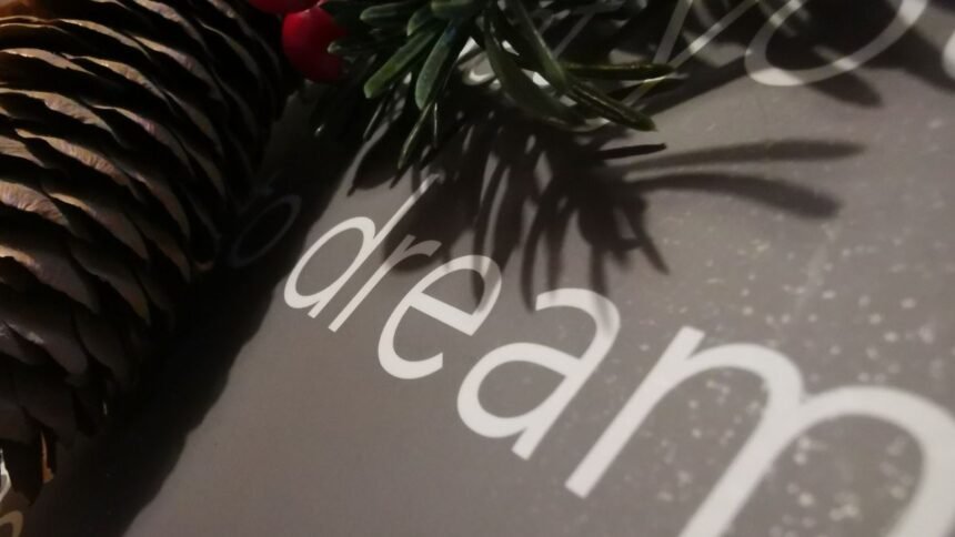 Fenyőtoboz és zöld levelek egy álomról szóló könyv melletti kompozícióban.