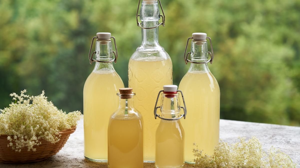 Házi bodzaszörp üvegek egy asztalon friss bodzavirágokkal