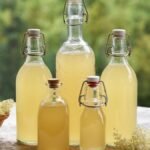 Házi bodzaszörp üvegek egy asztalon friss bodzavirágokkal